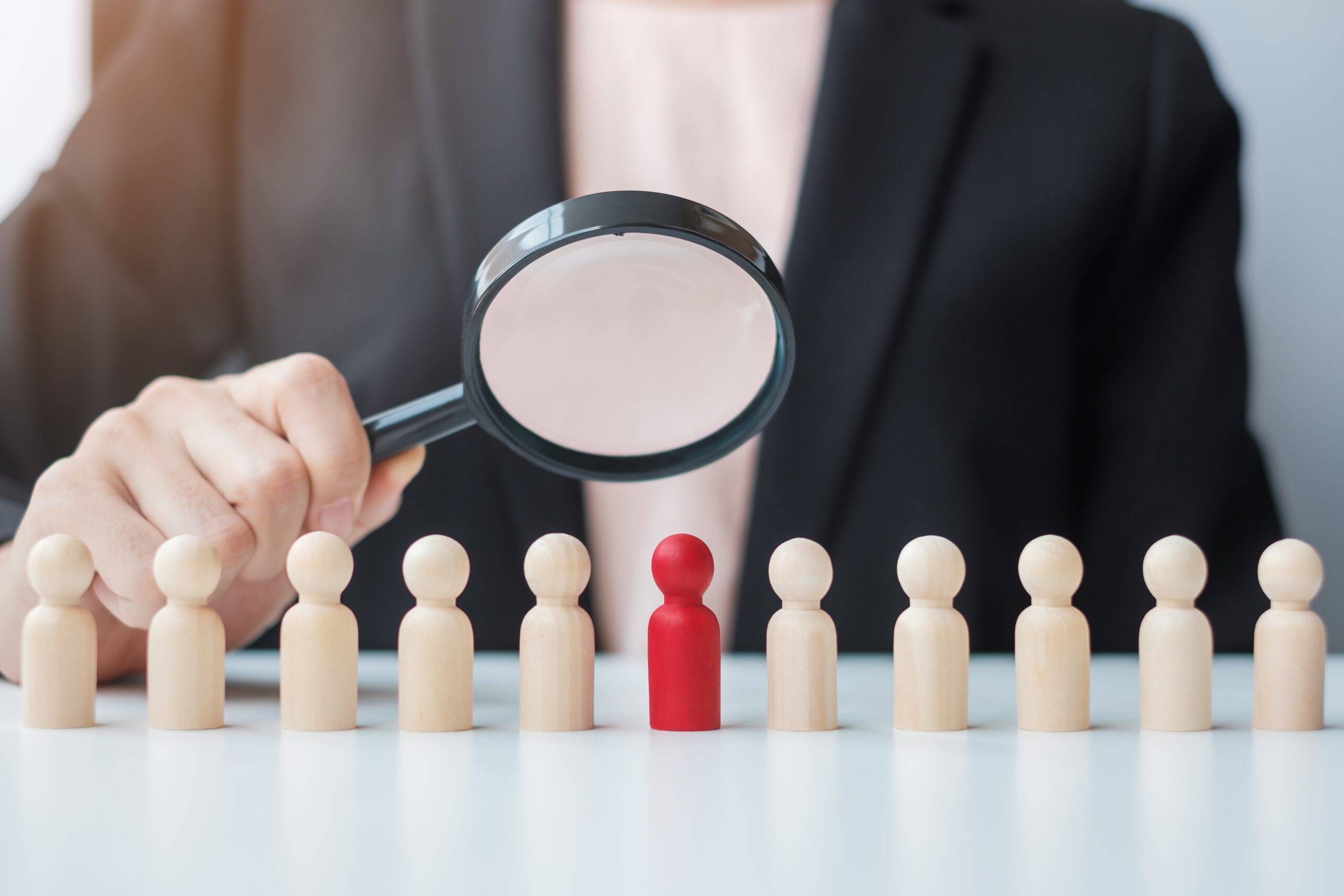Businesswoman hand holding magnifying glass for recruiting leader man wooden from crowd of employees.Human resource management, Recruitment, Teamwork, hiring and leadership Concepts